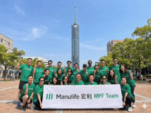 Group photo of a corporate team from Manulife standing in front of Fukuoka Tower during a company visit in Fukuoka.